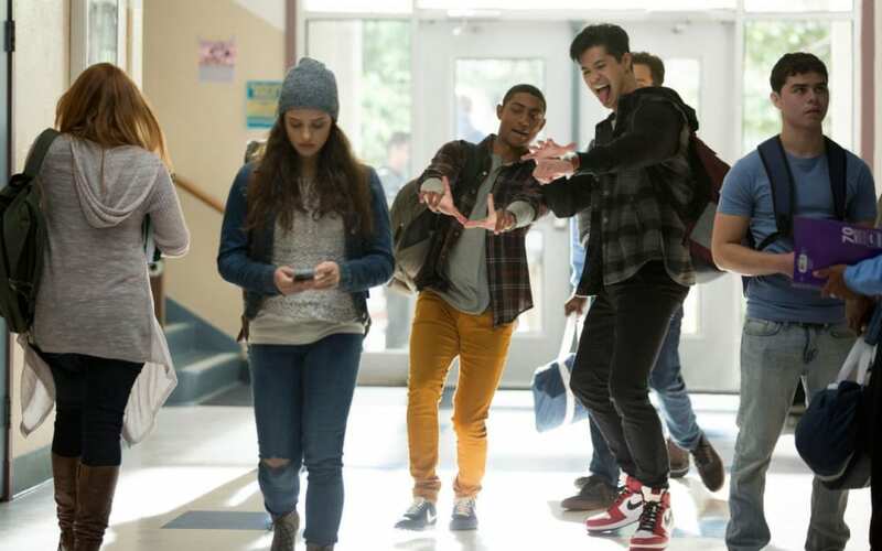 Cette image montre Hannah dans son établissement scolaire, et deux garçons, Marcus et Zach font des gestes obscènes derrière elle.