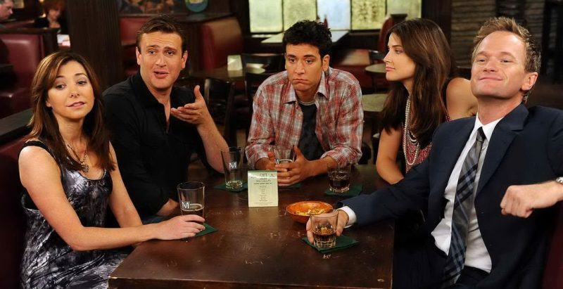 Les cinq protagonistes d'How I Met Your Mother : Lily, Marshall, Ted, Robin et Barney attablés au bar