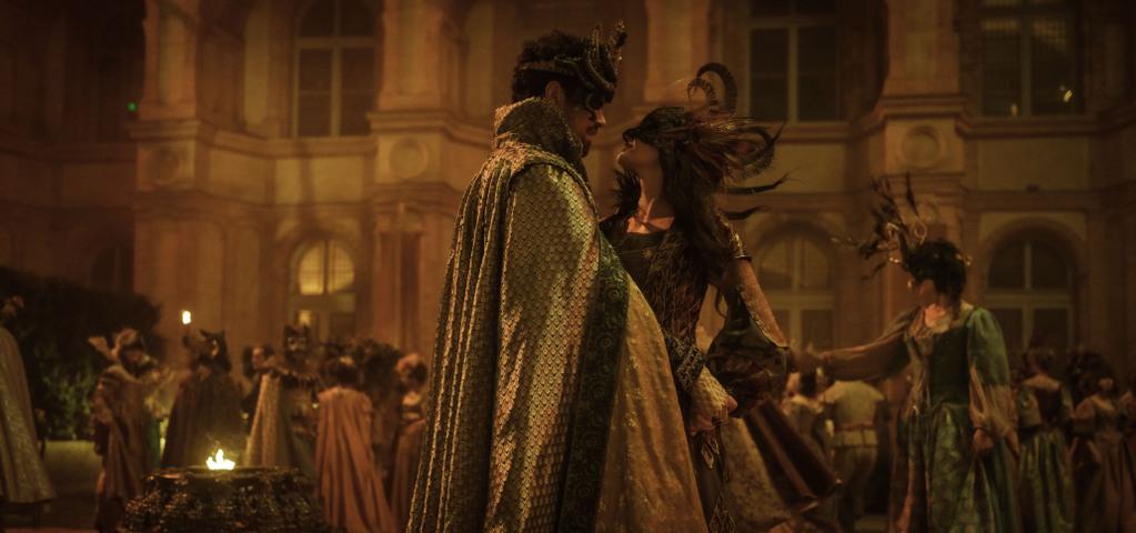 Un bal masqué devant un château style Renaissance. Un homme et une femme au premier plan (Buckingham et Milady) dansent ensemble. Ils sont masqués et déguisés, et semblent flirter.