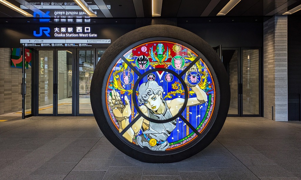 La sculpture ressemble à un vitrail sur lequel Araki a peint un personnage, et les têtes de plusieurs stands dans des bulles.