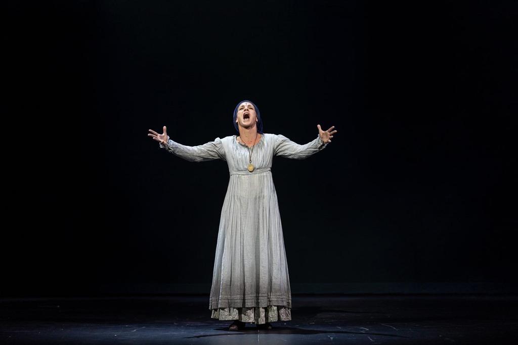 Fantine, en tenue d’ouvrière, chantant seule au milieu de la scène. Elle est vêtue de blanc et le décor est un fond noir.