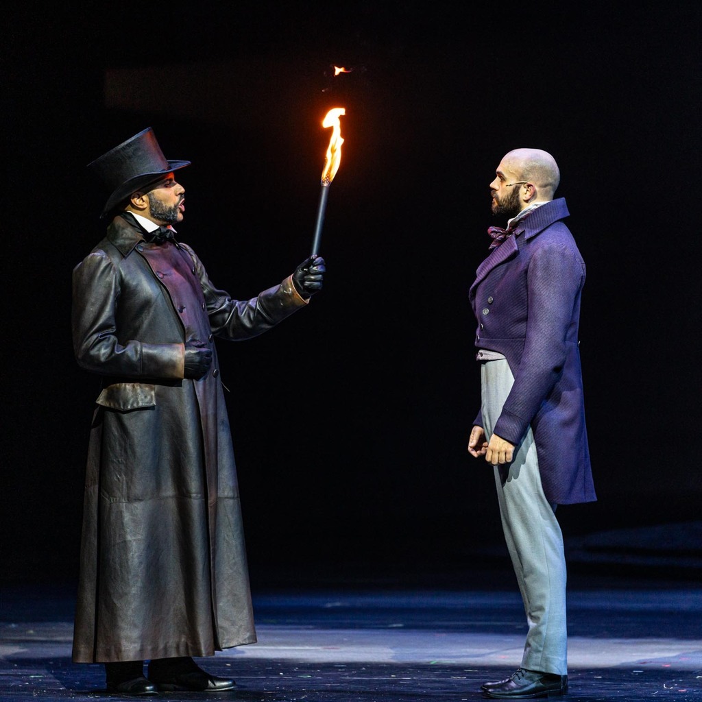 Javert et Jean Valjean face à face. Javert porte un imperméable en cuir, un haut de forme et tient une torche.