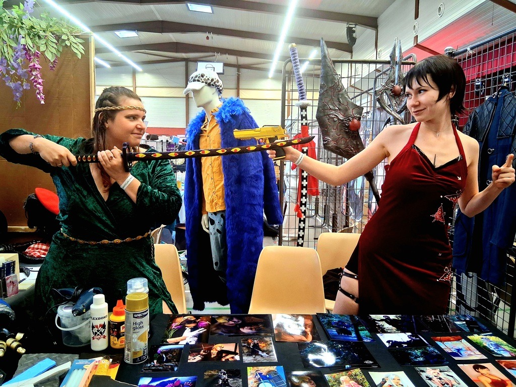 Ce sont deux femmes. L'une des deux est cosplayée en tueuse à gage et l'autre en loki, et l'une menace l'autre avec un revolver et l'autre un katana.