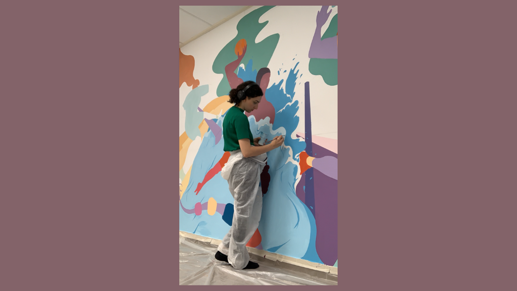 Yona Rouach en train de réaliser une fresque colorée avec un casque sur ses oreilles.
