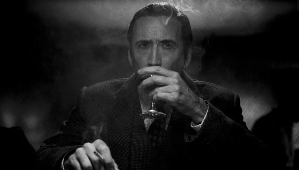 Un homme en costume (Nicolas Cage) boit son verre en fumant de l'autre main. Un air pensif (ou concentré ?). La scène est en noir et blanc.