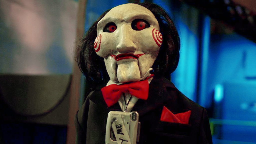 Petite marionnette aux yeux rouges. Dans le film, elle supervise les tortures.